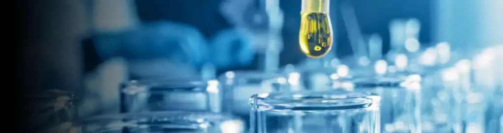 a close-up of a laboratory setting, with a dropper releasing a golden liquid into a glass container.